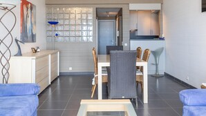 Een moderne woonkamer met een eethoek, een keuken en een groot raam met decoratieve zonwering.