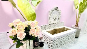 Une table ronde en verre, ornée d’un vase de roses roses, d’un petit flacon et d’une bougie.