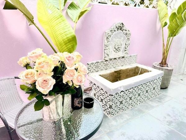 A round glass table with a vase of pink roses, a small bottle, and a candle. - The Villa Rosa Bed and Breakfast (Cape Town)