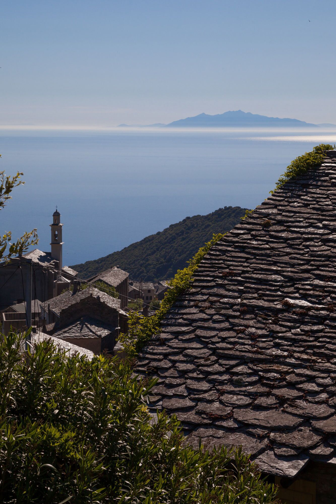 A stone roofed building with a view of the sea and mountains in the background.