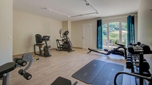 Un gimnasio con equipamiento de ejercicio, colchonetas y vistas a zonas verdes a través de amplias ventanas.