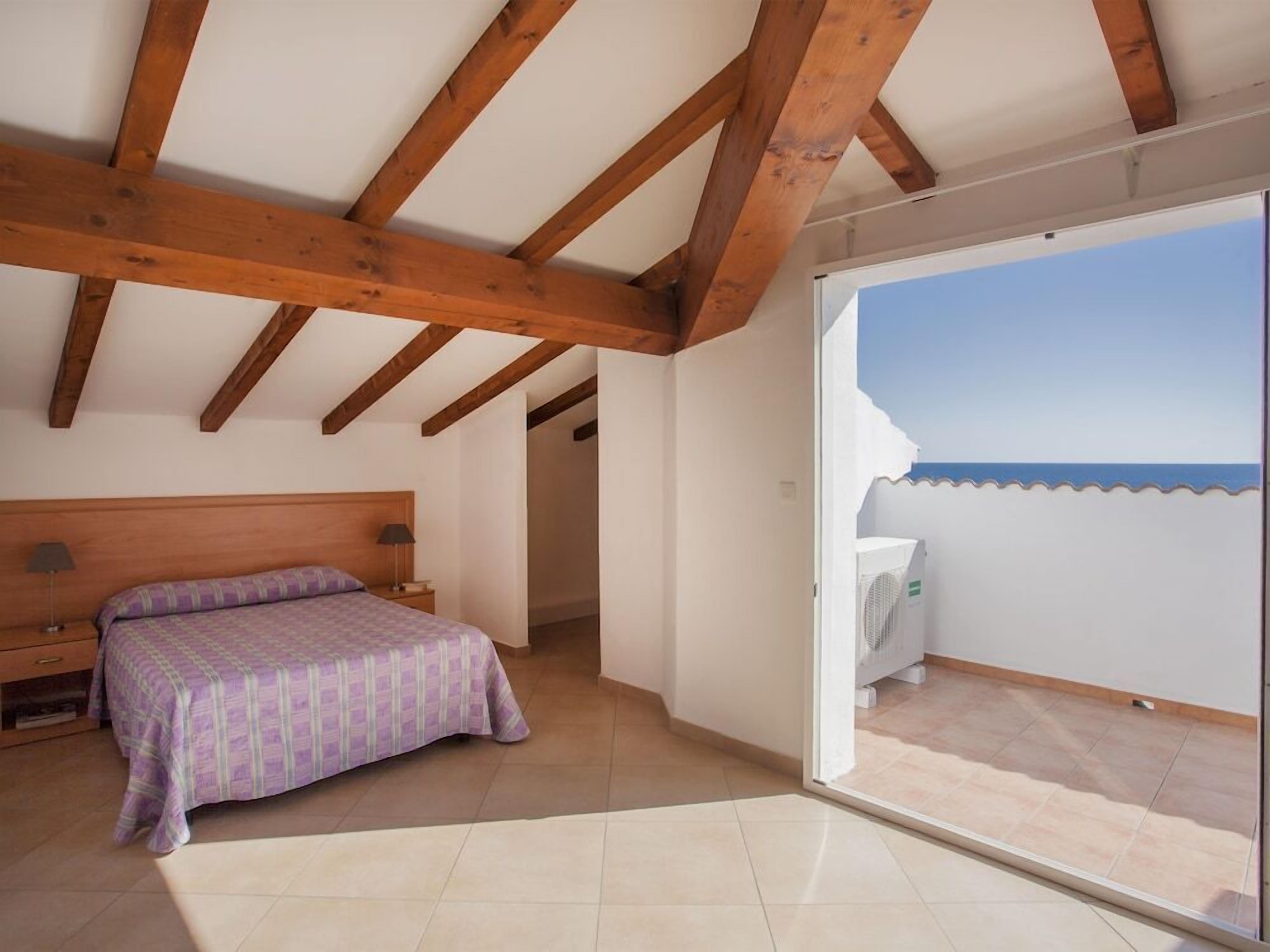 A bedroom with a bed, a nightstand, and a view of the sea through a sliding glass door.