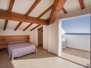 A bedroom with a bed, a nightstand, and a view of the sea through a sliding glass door. - Residence Sognu Di Rena (San-Nicolao)