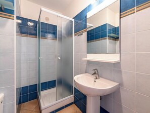 A bathroom with a glass-enclosed shower, a white sink, and blue-tiled walls. - Residence Sognu Di Rena (San-Nicolao)