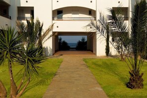 Un edificio moderno con una entrada central, rodeado de palmeras y un camino que lleva a la entrada.