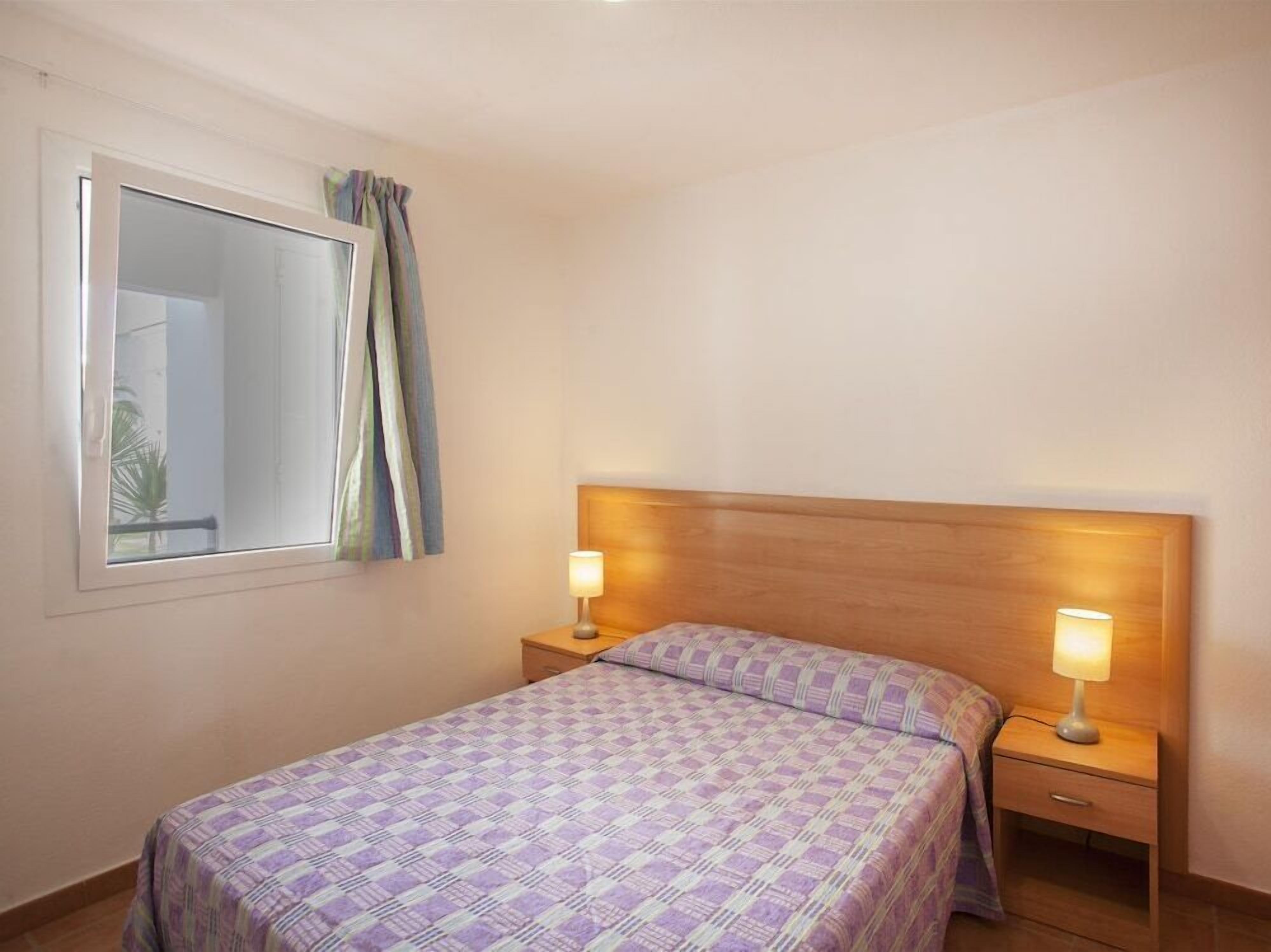 A bedroom with a bed, two bedside tables, a nightstand, a window with curtains, and a headboard.