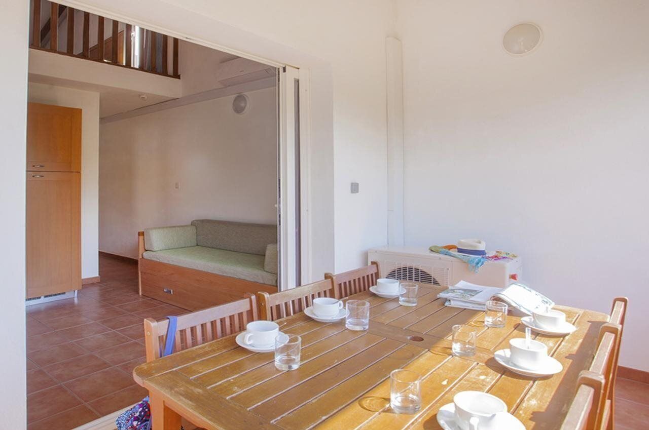 Un comedor con una mesa de madera dispuesta para cuatro personas, un sofá y una cocina con armarios y un lavabo.