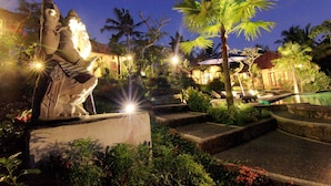A statue in a garden with palm trees and a pool. - Villa Capung Mas (Ubud)