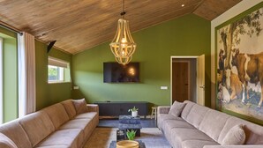 Ein geräumiges Wohnzimmer mit hoher Decke, einer großen Sofagarnitur, einem Couchtisch und einem an der Wand befestigten Fernseher.