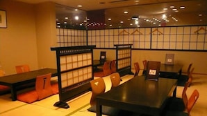 Una habitación al estilo japonés tradicional, con suelo de tatami, mesas bajas y sillas con cojines naranja.