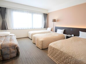 Habitación de hotel con dos camas, una mesita de noche, una lámpara, una ventana con cortinas y una alfombra estampada.
