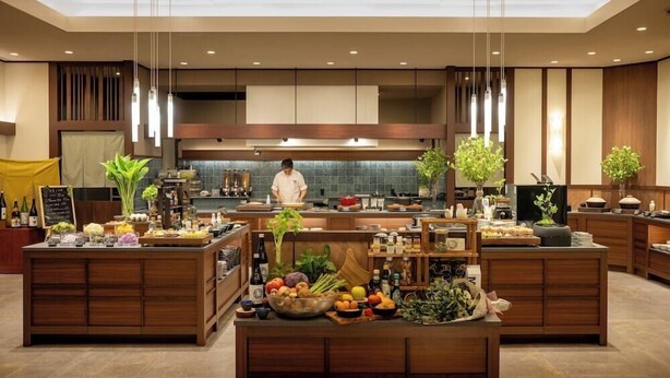 Cocina moderna con armarios de madera, una isla central con productos frescos y lámparas colgantes.