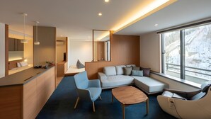Un interior moderno con un sofá, sillas, una mesa de centro, una zona de cocina y ventanas grandes.