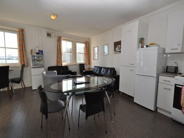 A modern kitchen with a dining area, white cabinets, a refrigerator, and a glass-top table with chairs.
