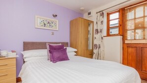Un dormitorio con cama, armario, mesita de noche, ventana con cortinas e imagen colgada en la pared.