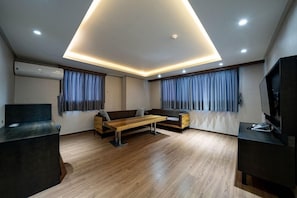 A modern living room with a wooden floor, a sofa, a coffee table, and a TV on a stand. - I-check Hyunjin Hotel (Donghae)