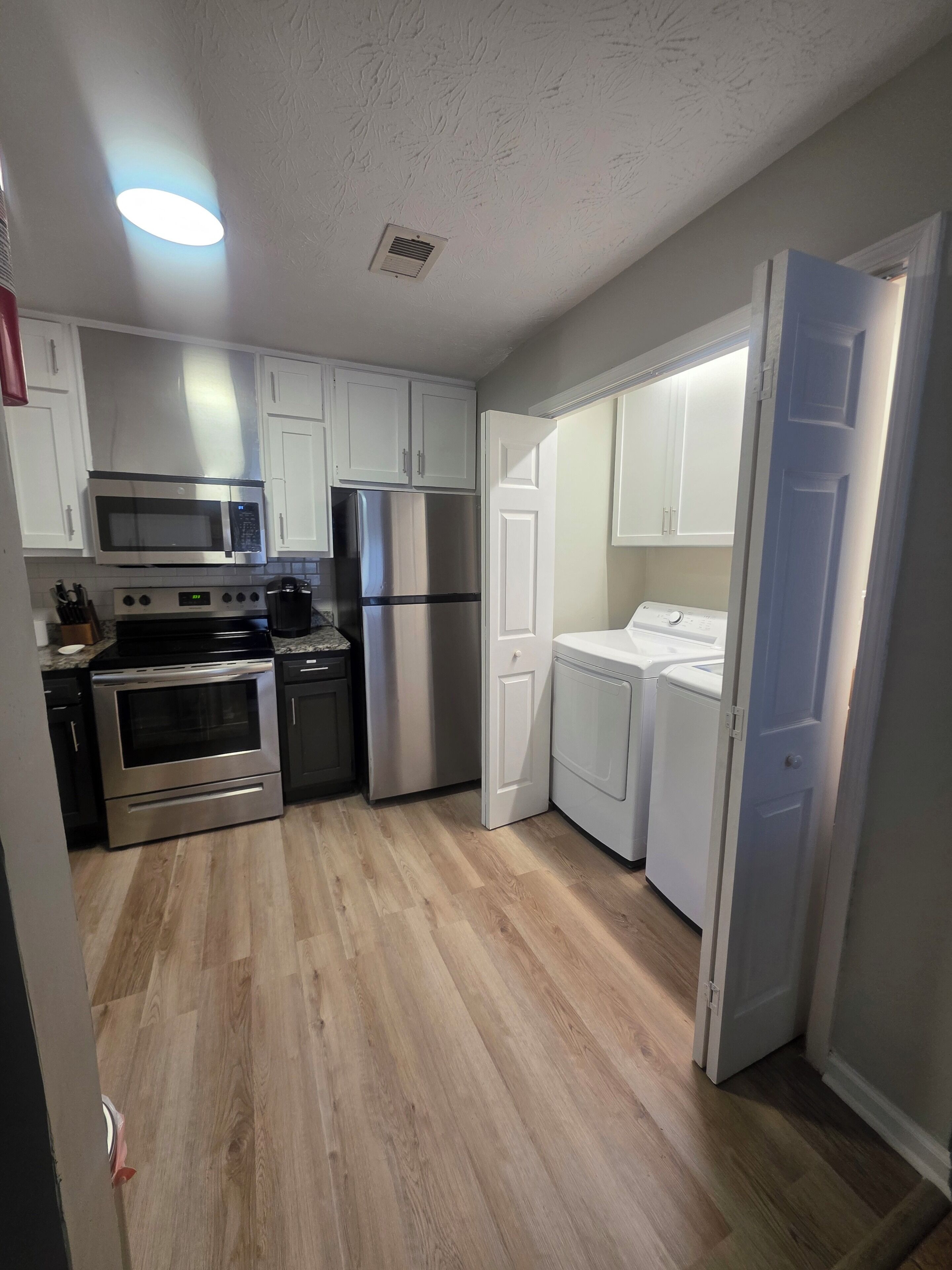 A compact kitchen with white cabinets, stainless steel appliances, and a wooden floor.