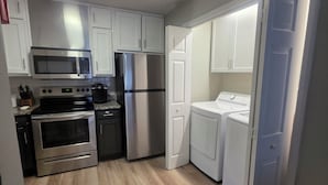 Una cocina funcional con armarios blancos, electrodomésticos de acero inoxidable y piso de madera.