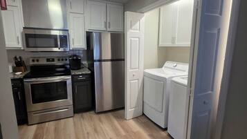 A compact kitchen with white cabinets, stainless steel appliances, and a wooden floor.