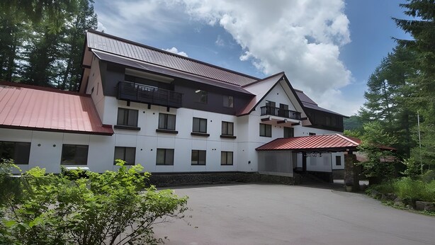 A modern two-story building with a red roof, surrounded by greenery and trees. - Izumigo Takayama Dog Paradise Hotel (Takayama)
