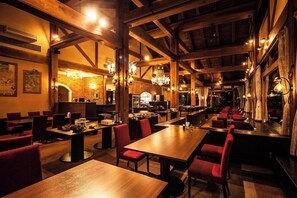 Un restaurante espacioso con altos techos de madera, varias mesas de comedor y sillas tapizadas en rojo.