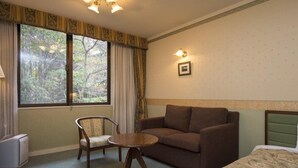 A hotel room with a brown sofa, a wooden chair, a small round table, and a bed with a floral bedspread. - Izumigo Takayama Dog Paradise Hotel (Takayama)