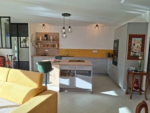 Une cuisine moderne avec un îlot central, un coin repas doté d’un canapé jaune et une petite table d’appoint en bois.