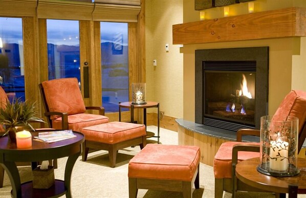 A cozy living room with a fireplace, comfortable seating, and a view through large windows. - Teton Springs Lodge And Spa (Victor)