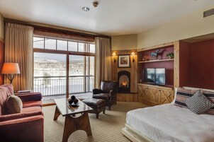 Una habitación de hotel con un ventanal grande, chimenea, televisor, sofá y cama.