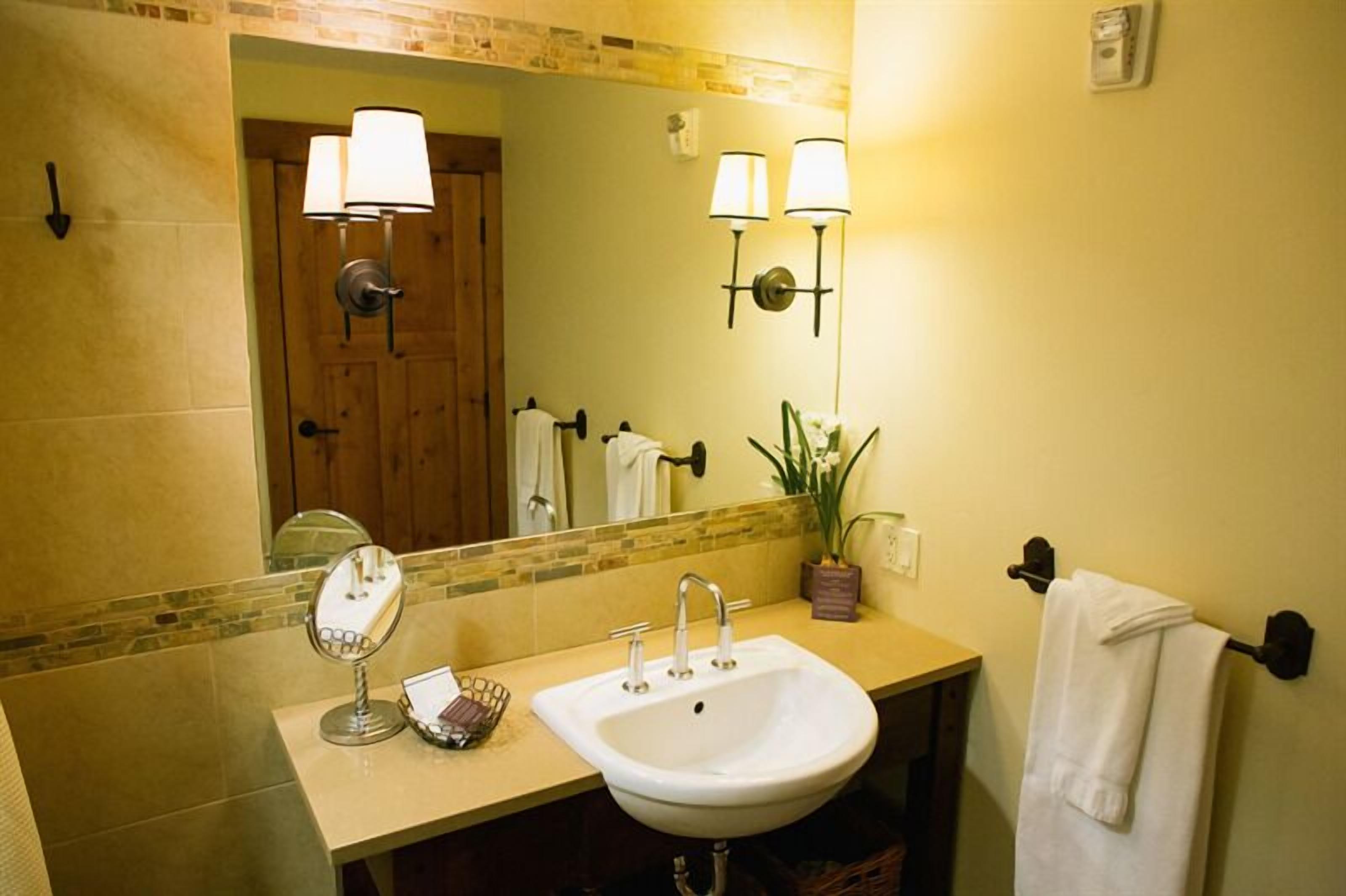 A bathroom with a sink, mirror, towel rack, and two wall-mounted lamps.