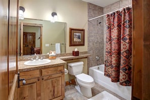 A bathroom with a wooden vanity, a sink, a toilet, a bathtub, and a shower curtain. - Teton Springs Lodge And Spa (Victor)