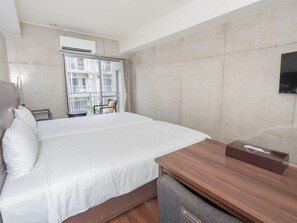 Habitació d'hotel amb un llit gran, una taula de fusta, televisió i una finestra amb vista a edificis.