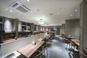 Un restaurante moderno con largas mesas de madera, una zona de cocina y un bar.