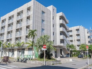 Um edifício moderno de vários andares com varandas, um sinal de proibido estacionar e uma área de estacionamento com scooters.
