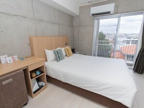 Una habitación de hotel moderna con una cama grande, un escritorio con silla, un armario pequeño y una ventana con vistas a la ciudad.