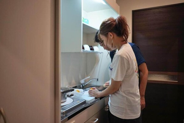 A person preparing food in a kitchen with a sink, countertop, and cabinets. - The Breakfast Hotel Porto Ishigaki (Ishigaki)