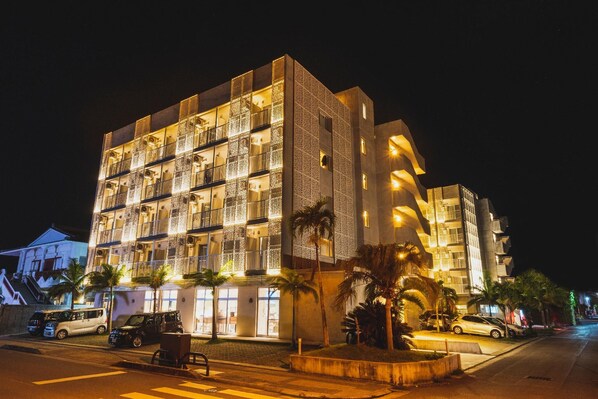 Hotel com vários andares, varandas, área de estacionamento e palmeiras.