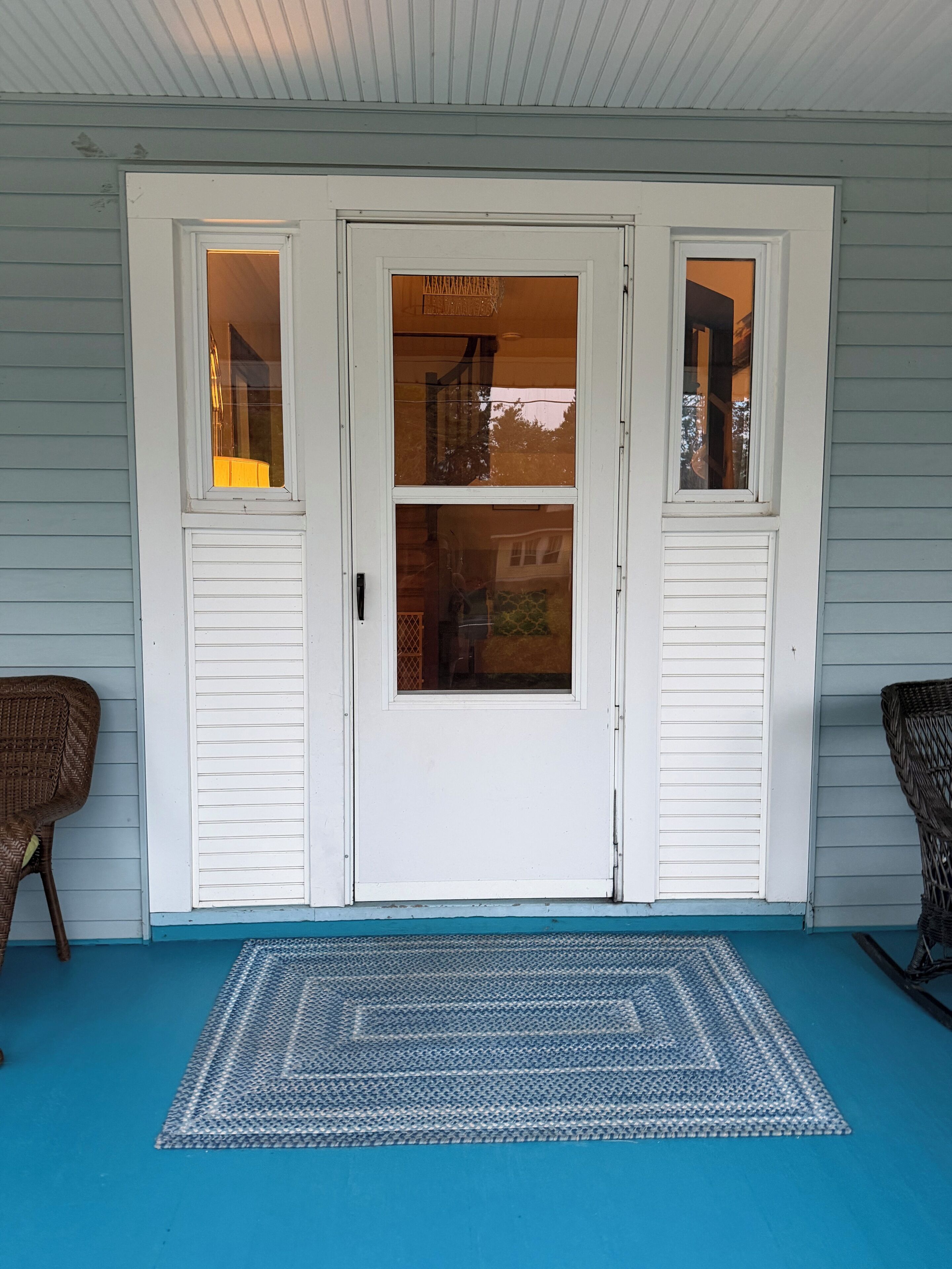 A front door with two side windows and a porch with a blue mat.