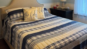Een slaapkamer met een bed, nachtkastje, lamp en wanddecoratie.
