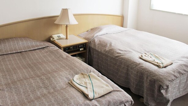 A hotel room with two beds, a bedside table with a lamp, a phone, and a folded towel on each bed. - Hotel Trend Mito (Mito)