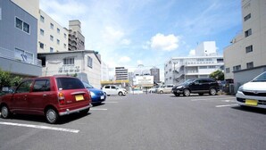 A parking lot with various cars, including a red car and a white car, and buildings in the background. - Hotel Trend Mito (Mito)