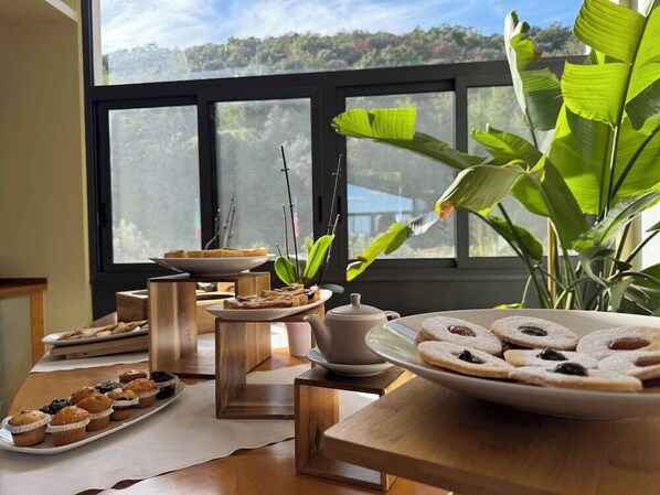 A breakfast setup with pastries and a teapot on a wooden table near a window with a view of trees. - LH Hotel Del Lago Bracciano (Bracciano)