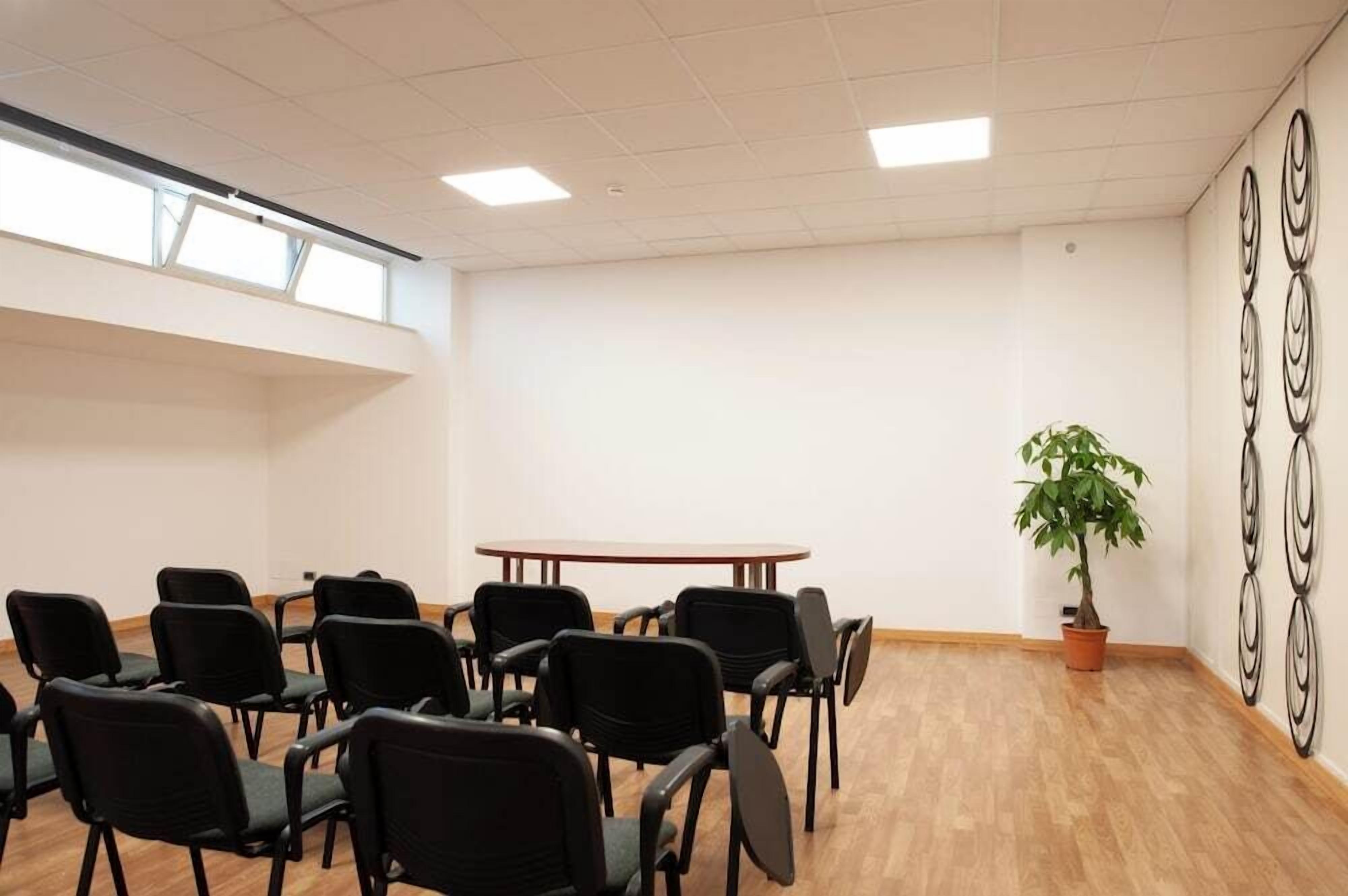 Une salle de conférence avec une table ronde et des chaises noires, une plante en pot et un élément décoratif mural.