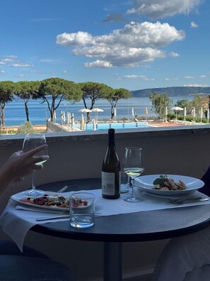 Ein Esstisch mit einer Weinflasche, Gläsern und Tellern voller Speisen, mit Blick auf einen Pool und Bäume.