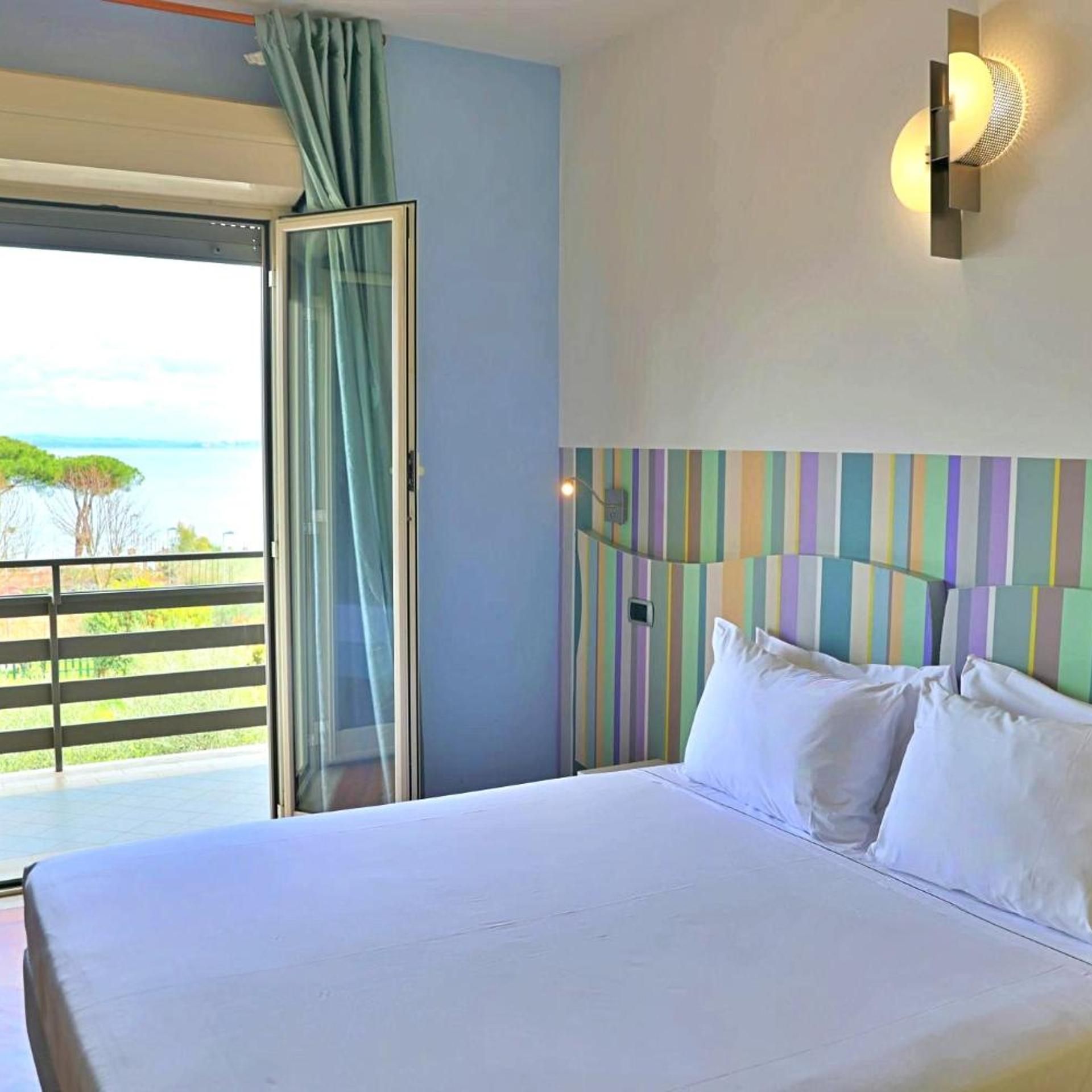 Una habitación de hotel con cama, vista al mar y balcón con barandilla.