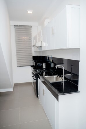 A modern kitchen with white cabinets, a black countertop, stainless steel appliances, and a window with blinds.