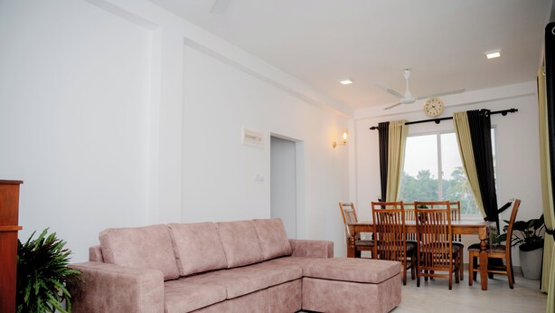 Ein Wohnzimmer mit einem rosa Modularesofa, einem Esstisch mit Stühlen, einem Deckenventilator und einem Fenster mit Vorhängen.