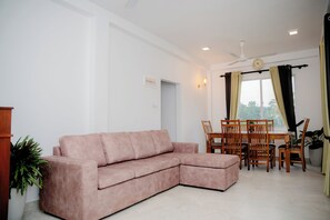 Sala de estar com um sofá seccional rosa, uma mesa de jantar com cadeiras, um ventilador de teto e uma janela com cortinas.