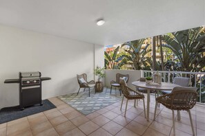 Un balcón con una parrilla, sillas de mimbre, una mesa y vistas a palmeras.