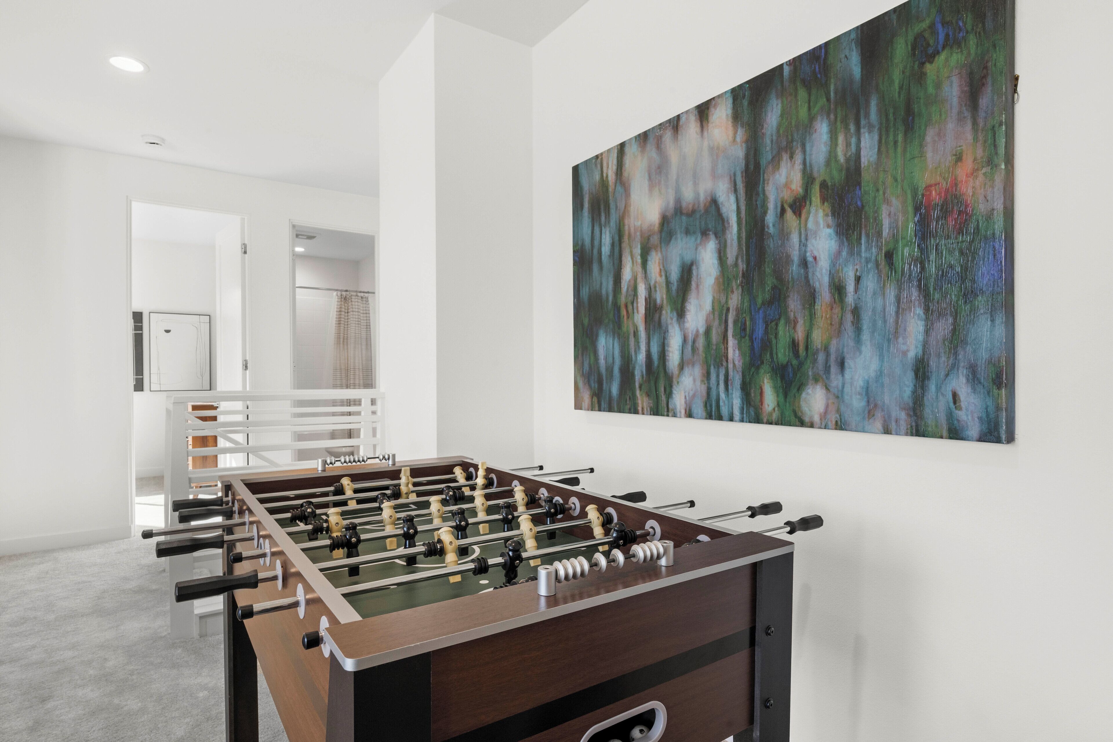 A modern room with a foosball table, a large abstract painting, and a kitchen area in the background.